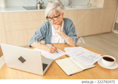 Middle aged senior woman using laptop computer writing notes at home. Focused mature old businesswoman work in home office making written records doing online work. Mature boss professional worker Middle aged senior woman using laptop computer writing notes at home. Focused mature old businesswoman work in home office making written records doing online work. Mature boss professional worker 122792072