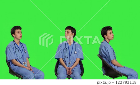 Medical assistant is waiting for patients to attend exam appointments, feeling impatient while she sits in a chair. Nurse with stethoscope and scrubs waits for people against greenscreen. Camera B. 122792119