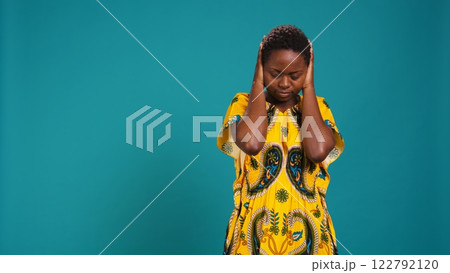 Moral person doing three wise monkeys symbol in studio, covering her eyes, mouth and ears against blue background, See no evil, speak no evil and hear no evil metaphor, wisdom concept. Camera B. 122792120