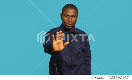 Security guard doing stop sign gesturing, being tasked with preventing criminal activity and detaining suspects. Portrait of stern bodyguard showing halt hand gesture, studio background, camera A Security guard doing stop sign gesturing, being tasked with preventing criminal activity and detaining suspects. Portrait of stern bodyguard showing halt hand gesture, studio background, camera A 122792147