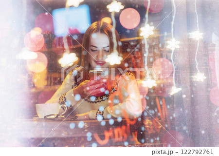 Young beautiful woman sitting in cafe, drinking coffee. Christmas, new year, winter holidays concept double exposure, night city 122792761