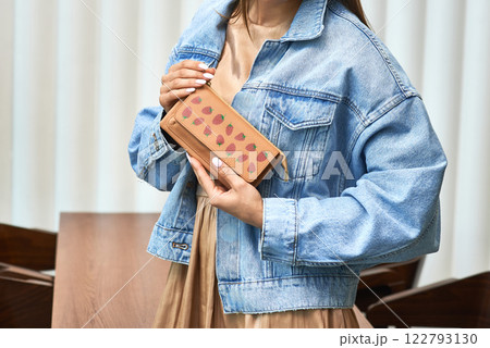 Stylish woman holding strawberry patterned wallet in casual denim outfit, simple wooden table background, fashion accessory concept Stylish woman holding strawberry patterned wallet in casual denim outfit, simple wooden table background, fashion accessory concept 122793130