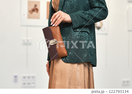 Elegantly dressed woman holding a stylish leather clutch purse in a modern art gallery setting, fashion concept 122793134