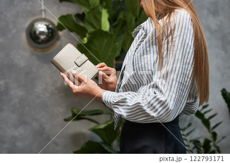 Elegant woman in striped blouse holding stylish leather wallet in indoor greenery setting, sophisticated fashion concept Elegant woman in striped blouse holding stylish leather wallet in indoor greenery setting, sophisticated fashion concept 122793171