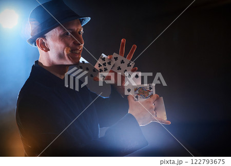 Magician showing trick with playing cards. Magic or dexterity, circus, gambling. Prestidigitator in dark room with fog 122793675