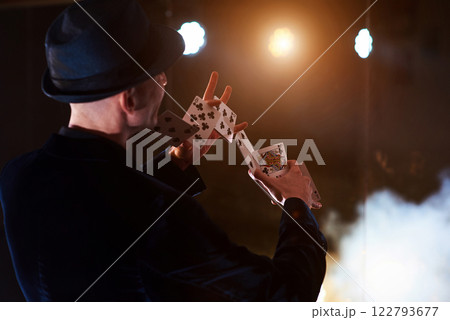 Magician showing trick with playing cards. Magic or dexterity, circus, gambling. Prestidigitator in dark room with fog 122793677