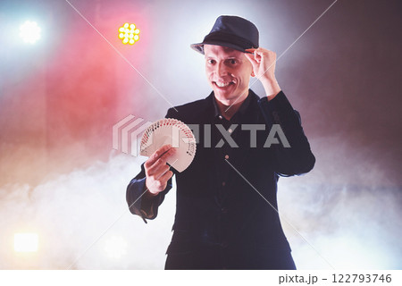 Magician showing trick with playing cards. Magic or dexterity, circus, gambling. Prestidigitator in dark room with fog 122793746