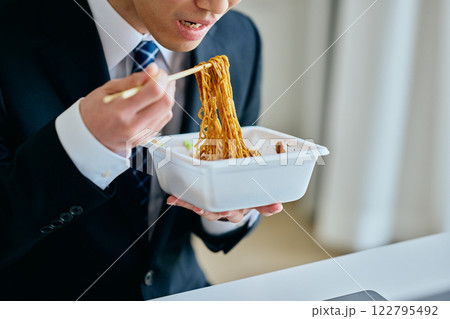 カップ焼きそばを食べながら仕事をする20代の若い男性 カップ焼きそばを食べながら仕事をする20代の若い男性 122795492