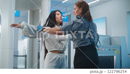 Female Security Officer Checks Woman After Metal Detector Scanning Gates 122796254