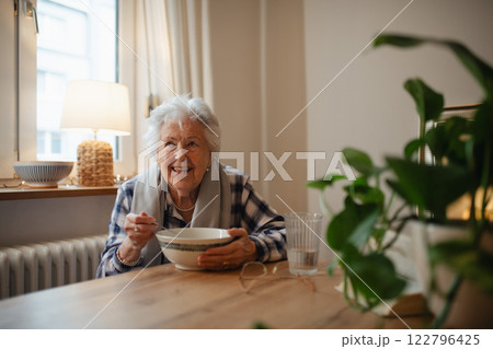 Poor elderly woman eating soup at the dining table. Poor elderly woman eating soup at the dining table. 122796425
