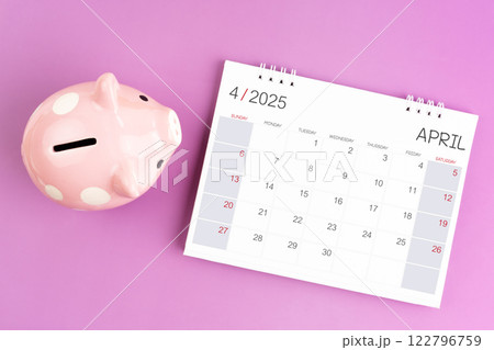 Desk calendar for April 2025 and pink piggy bank on purple background. 122796759