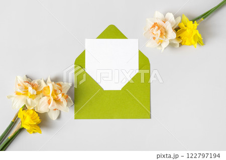 Green envelope with clean white sheet of paper for your text and spring flowers white tulips and daffodils on gray background. Invitation to the holidays. Hello spring 122797194