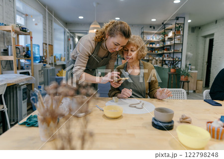 Happy retired student learns new skills, creating a handmade ceramic bowl. Female artist teaches an elderly woman how to shape clay at a hands-on master class 122798248