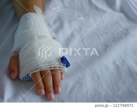The patient's hand is wrapped in white bandages and has a saline line. The patient's hand is wrapped in white bandages and has a saline line. 122798972