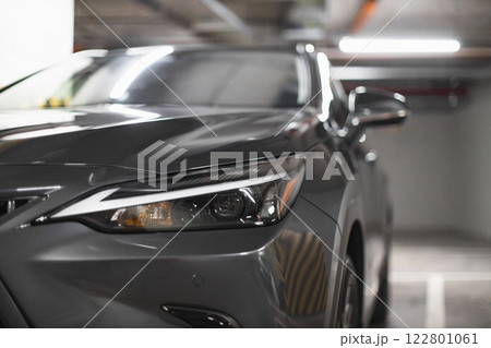 Close-up of front headlight on sleek modern car in underground parking lot showcasing design and style. Close-up of front headlight on sleek modern car in underground parking lot showcasing design and style. 122801061