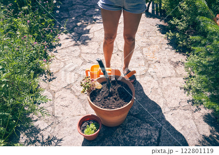 A woman's feet near a pot of earth. When transplanting plants, it is necessary to water the soil. The brunette is going to transplant plants into a clay pot. High quality photo A woman's feet near a pot of earth. When transplanting plants, it is necessary to water the soil. The brunette is going to transplant plants into a clay pot. High quality photo 122801119