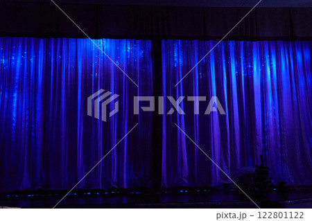 A stage with closed curtains, waiting for the artists to perform. Blue lamps are shining on the stage. With space to copy. High quality photo 122801122