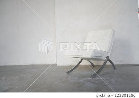 A white leather armchair with metal legs stands in an empty room against the background of a concrete wall. With space to copy. High quality photo A white leather armchair with metal legs stands in an empty room against the background of a concrete wall. With space to copy. High quality photo 122801186
