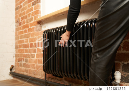 There is a problem with central heating in the house. A woman checks the radiator in a cold apartment. High quality photo 122801233
