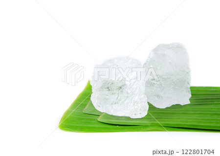 Pieces of white alum sit on a banana leaf, set against a white background. This simple yet meaningful display represents the use of natural minerals in purification, skincare, and household remedies. Pieces of white alum sit on a banana leaf, set against a white background. This simple yet meaningful display represents the use of natural minerals in purification, skincare, and household remedies. 122801704