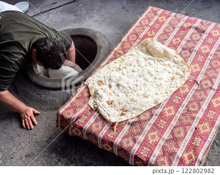 woman glues raw dough for lavash in tandoor 122802982