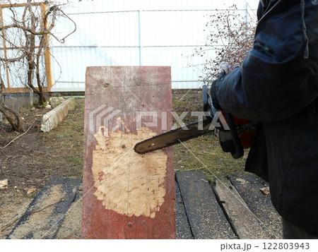 sawing out a part of a board with a chainsaw in a carpenter's shop outside, cutting off chips from a solid old board with a chainsaw blade to create a designer object outdoor 122803943
