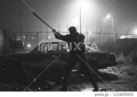 Hooligan attacking parked car with a bat in an urban environment at night 122804005