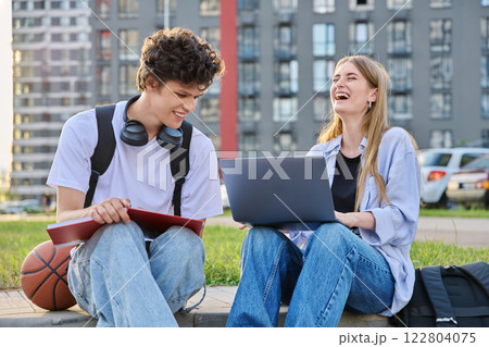 Teenage college students guy and girl laughing having fun together, sitting outdoor 122804075