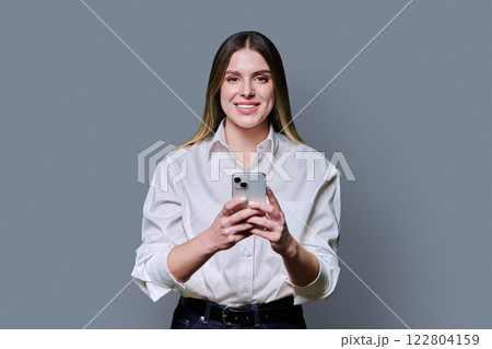 Young beautiful woman holding mobile phone, looking at camera on grey studio background Young beautiful woman holding mobile phone, looking at camera on grey studio background 122804159