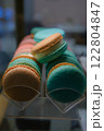 Close-up of colorful macarons with white cream filling displayed under soft lighting on a countertop with a blurred background and selective focus highlighting their delicate texture and vibrant hues 122804847