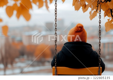 A child sits on a swing, gazing at an autumnal city view, lost in thought 122805135