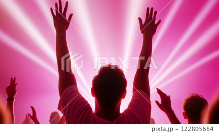 Concertgoers cheer with arms raised, immersed in vibrant pink neon lights and rhythm 122805684
