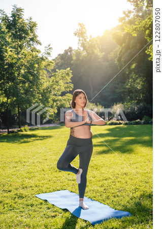 Pregnant caucasian woman standing in a tree pose and keeping her balance Pregnant caucasian woman standing in a tree pose and keeping her balance 122807050