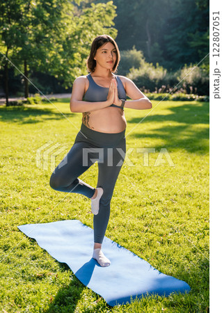 Pregnant caucasian woman standing in a tree pose and keeping her balance Pregnant caucasian woman standing in a tree pose and keeping her balance 122807051