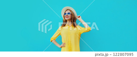 Beautiful young woman posing wearing summer straw hat, yellow shirt on blue studio background 122807095