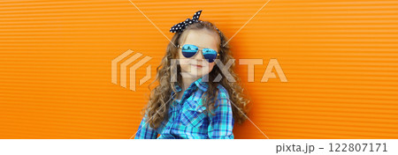 Happy kid girl with curly hair, stylish little child posing in the city on orange wall 122807171