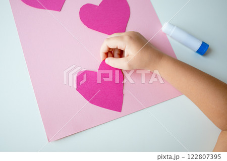 Child creating pink heart craft on pink paper Child creating pink heart craft on pink paper 122807395