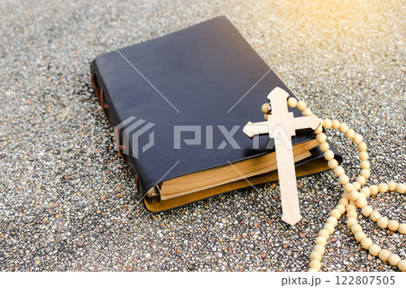 A white ivory cross placed on a dark brown notebook reflects purity, peace, and divine guidance. The contrast symbolizes light amidst darkness, faith, and personal devotion. 122807505