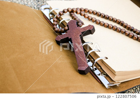 A simple wooden cross lies on an open brown notebook, signifying humility, faith, and a connection to spirituality. This evokes thoughts of prayer, scripture study, and religious dedication. 122807506