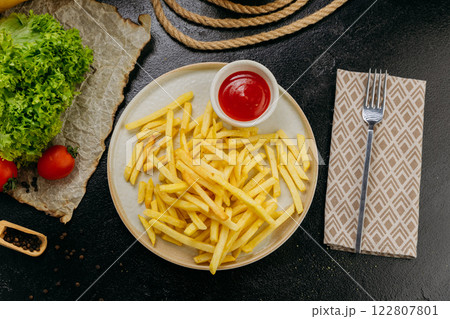 Crispy golden french fries with ketchup, served on a plate in a stylish restaurant setting 122807801