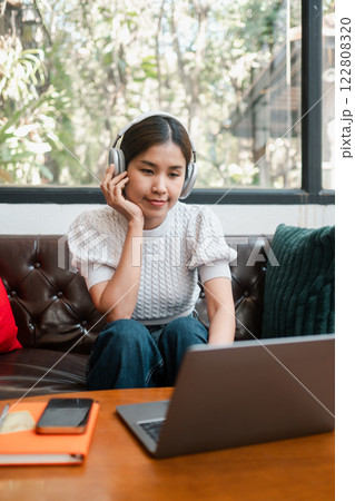 Woman enjoying music with headphones while working on a laptop in a stylish living room. Comfortable and modern setting. Woman enjoying music with headphones while working on a laptop in a stylish living room. Comfortable and modern setting. 122808320