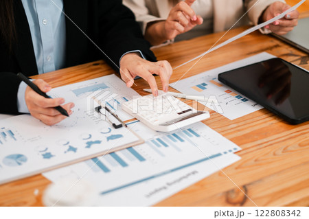 Close-up of hands using a calculator with financial charts and graphs on a wooden desk during a business meeting. 122808342