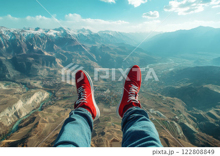 Aerial view of majestic mountain landscape with snow-capped peaks and red sneakers dangling over serene valley and river 122808849
