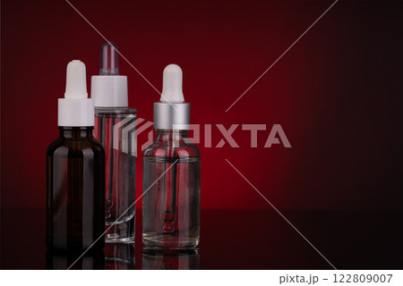 Three Glass Dropper Bottles with Different Designs on Red Background 122809007