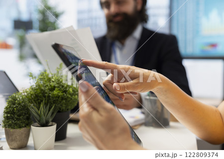 Financial advisor guiding clients in trading shares using software on tablet, making informed investment decisions. Agent offering advice on buying and selling stocks on device online, close up Financial advisor guiding clients in trading shares using software on tablet, making informed investment decisions. Agent offering advice on buying and selling stocks on device online, close up 122809374