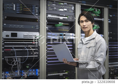 サーバーエンジニア　イメージ　カメラ目線のパソコンを持った作業服姿の若いエンジニア 122810608
