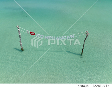 Koh Phangan sign suspended between wooden poles above tranquil turquoise waters. Ko Pha Ngan, Thailand. Koh Phangan sign suspended between wooden poles above tranquil turquoise waters. Ko Pha Ngan, Thailand. 122810717