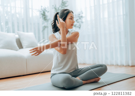 Happy young Asian woman practicing yoga and shoulder stretching at home 122811382