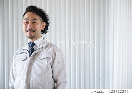工場の前で作業着姿の髭のカメラ目線の男性 122812242