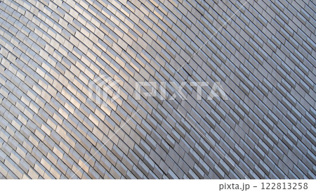 A sleek, silvery facade featuring a wave-like arrangement of metallic tiles, creating a harmonious blend of texture and reflection. 122813258